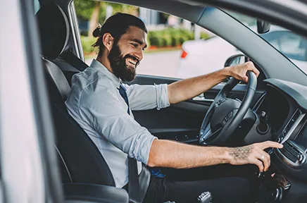 Ein lächelnder Mann mit Bart sitzt am Steuer eines Autos und bedient das Touchscreen-Display, während er fährt.