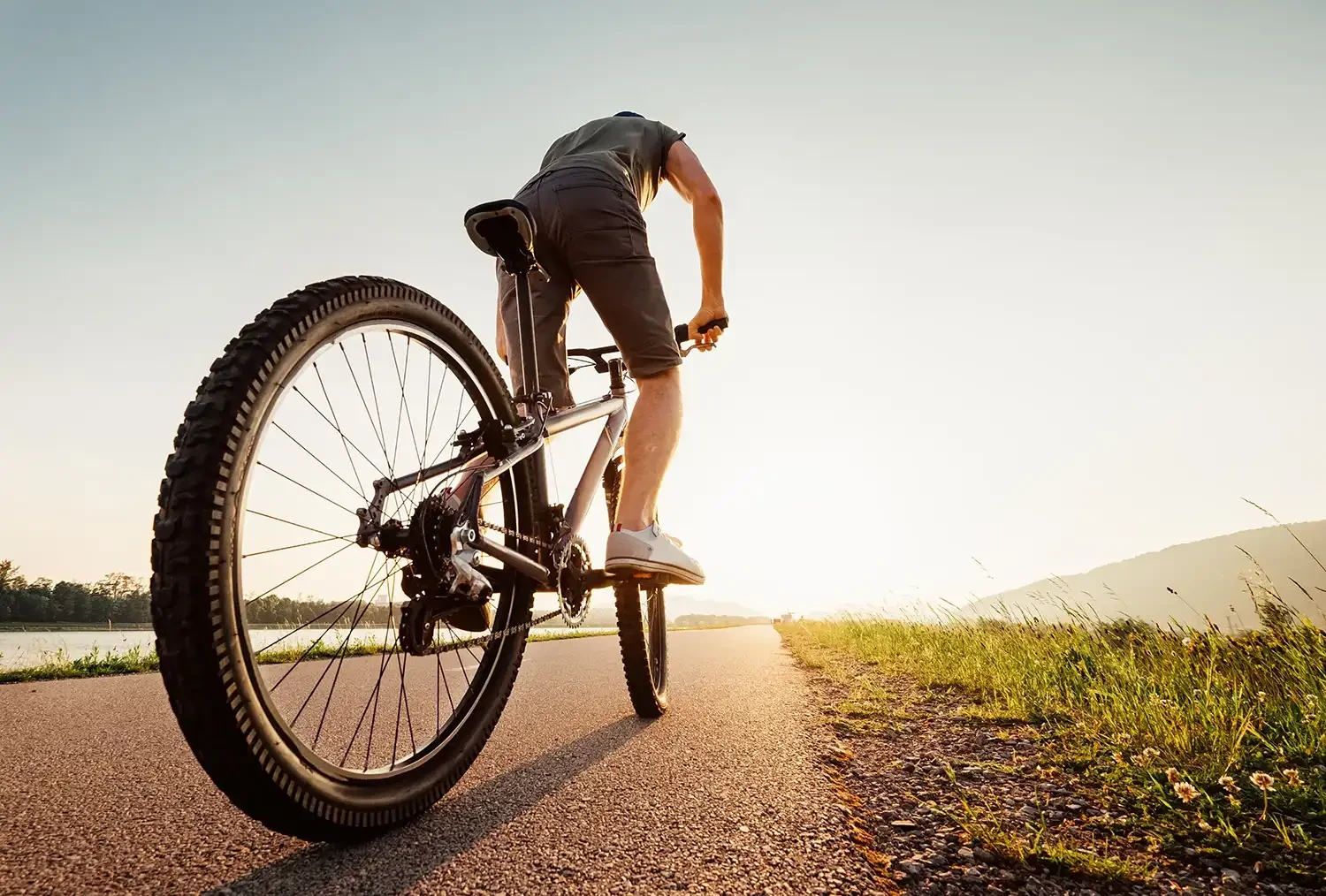 Mountainbiker auf einem Radweg bei Sonnenuntergang, mit Blick auf nahegelegenen See und Berge im Hintergrund.