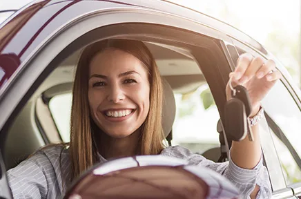 Eine lächelnde Person sitzt im Auto und hält einen Autoschlüssel hoch, bereit für die Fahrt.