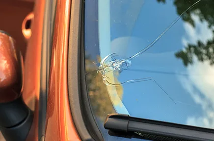 Ein Steinschlag hat eine sternförmige Beschädigung in der Windschutzscheibe eines orangefarbenen Autos verursacht.