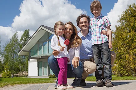 Glückliche vierköpfige Familie posiert vor ihrem modernen Einfamilienhaus mit Garten an einem sonnigen Tag.